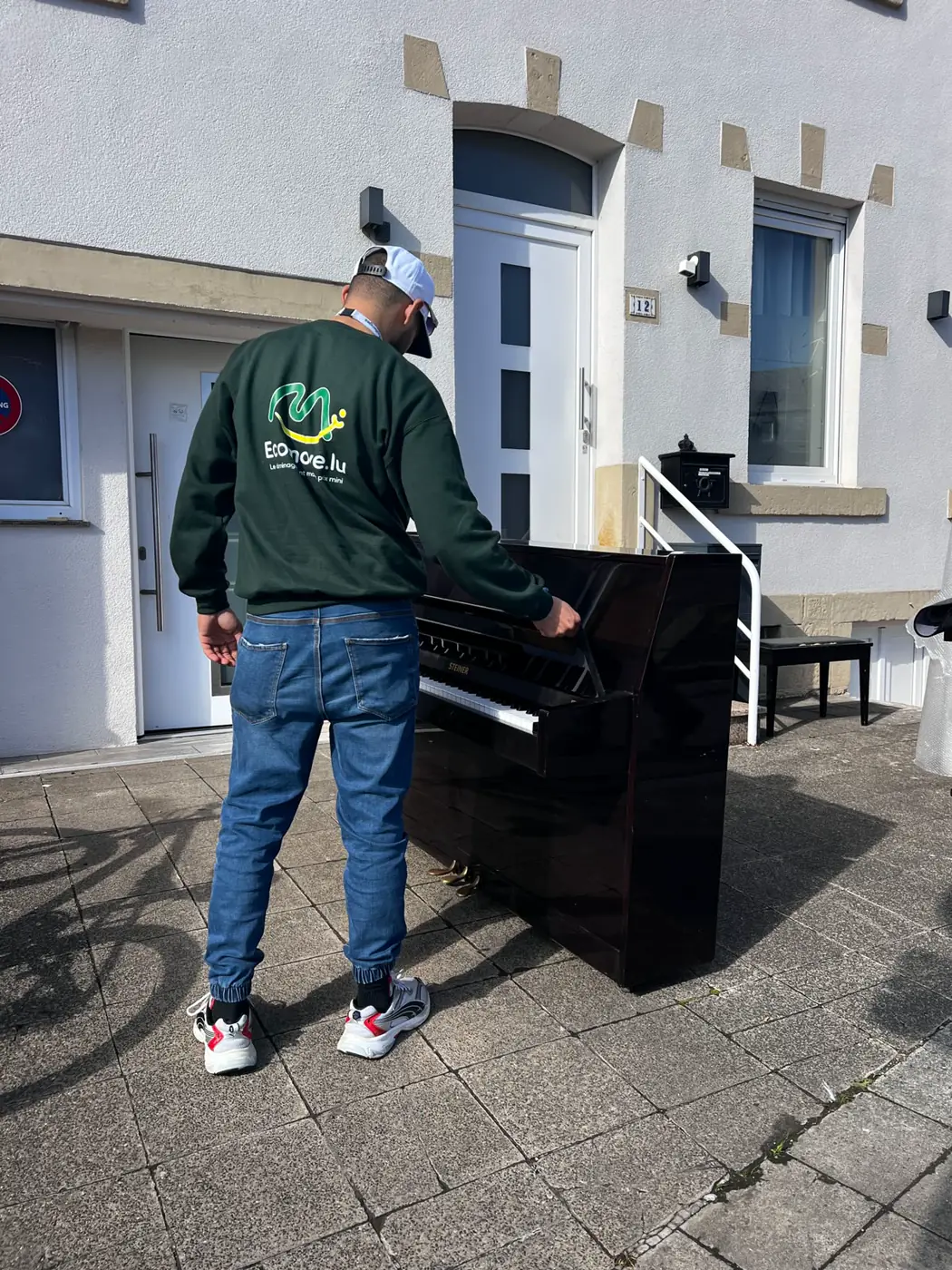 Déménageur Ecomove manipulant un piano devant une maison